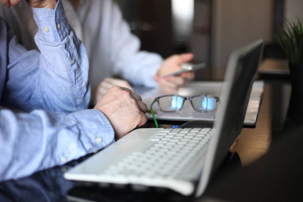 elderly man using laptop with glasses set aside to use screen reader